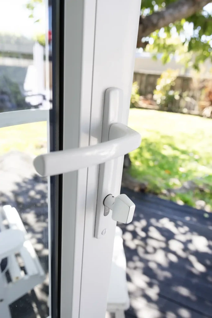close-up of white uPVC door handle and lock with garden background Christchurch