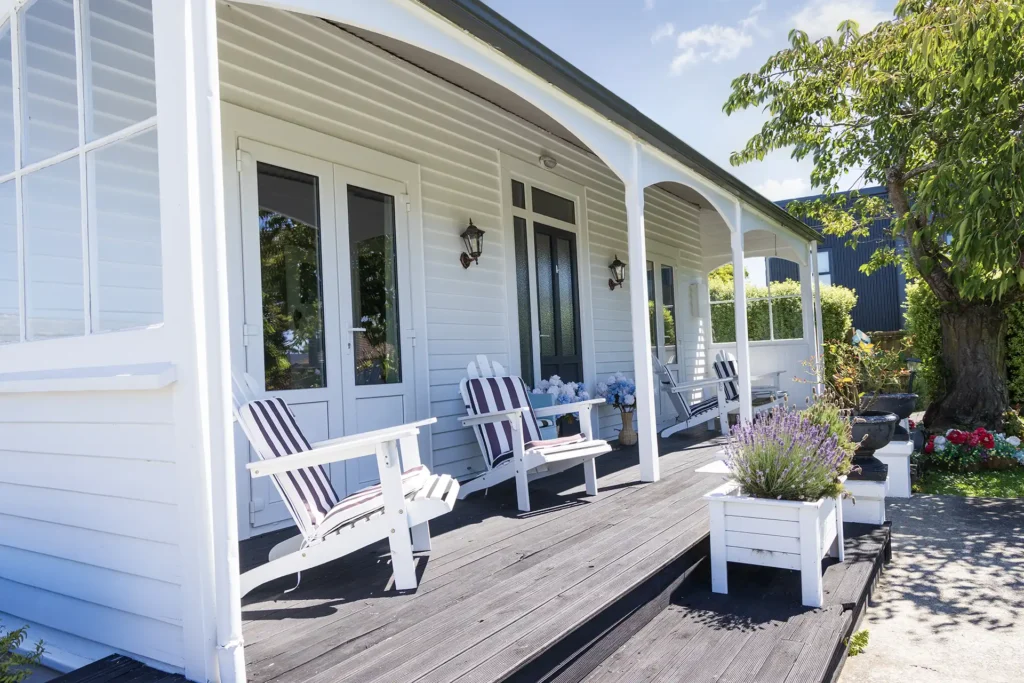 Classic Christchurch villa exterior with white weatherboards, uPVC double-glazed French doors, and a covered veranda with outdoor seating